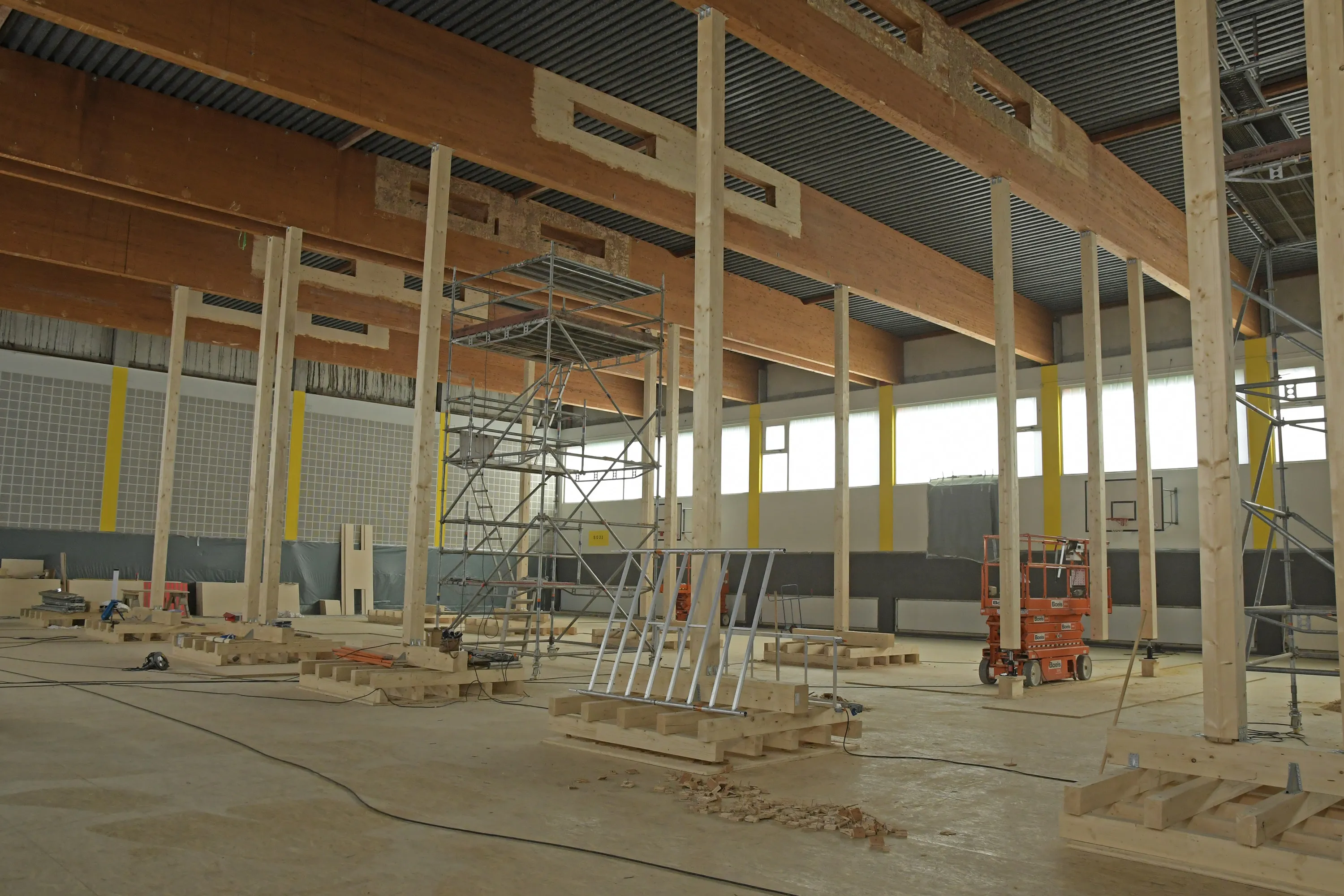 Rohbau einer Turnhalle mit sichtbaren Holzbalken und Gerüsten, während der Sanierung.