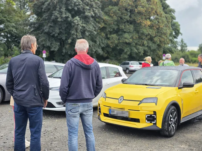 Zwei Männer betrachten einen gelben Renault bei einem Aktionstag, im Hintergrund stehen weitere Personen und Fahrzeuge.