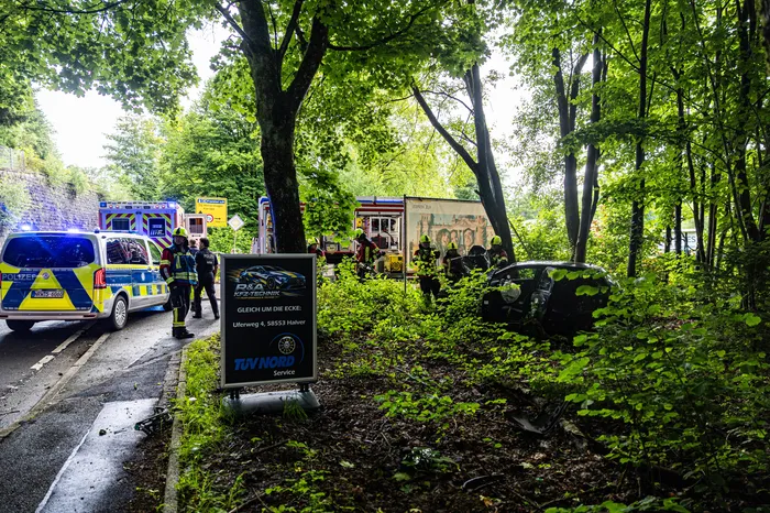 Polizeiauto und Rettungswagen sind an einem Unfallort in einer grünen Umgebung zu sehen. Im Vordergrund steht ein Werbeschild für eine Kfz-Technik und TÜV Nord.