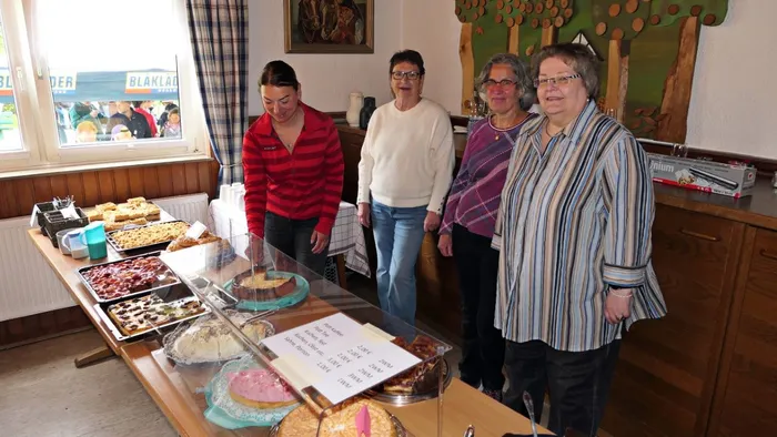 Vier Frauen betrachten ein reich gedecktes Buffet mit Kuchen und Gebäck in einem Wanderheim.