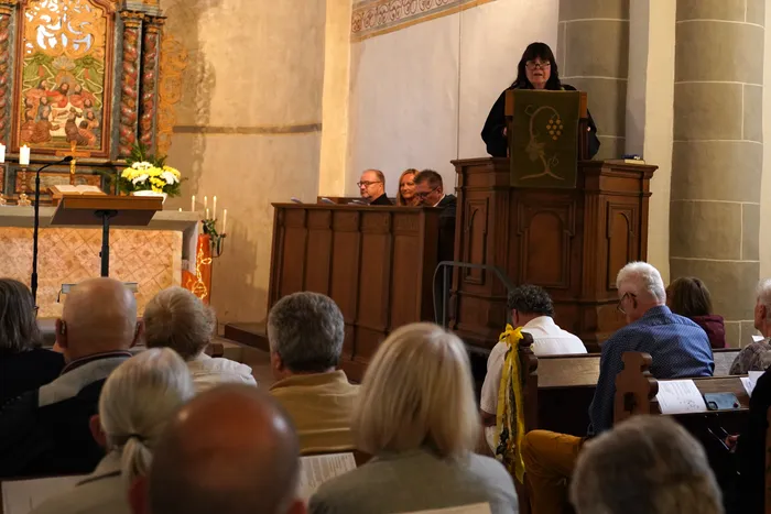 Pfarrerin Anju Laddach spricht von einer hölzernen Kanzel in einer Kirche vor einer sitzenden Gemeinde.