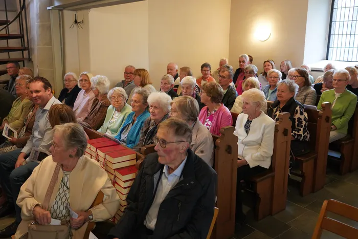 Eine Gruppe von Menschen sitzt in Holzbänken in einer Kirche während einer feierlichen Verabschiedung.
