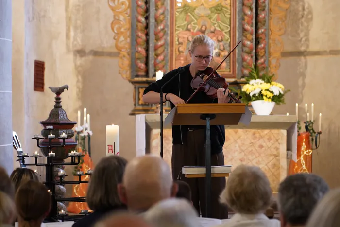 Eine Frau spielt Geige in einer Kirche vor einem Altar und einem Publikum.