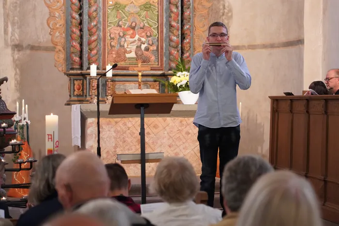 Ein Mann spielt Mundharmonika in einer Kirche während einer feierlichen Verabschiedung.