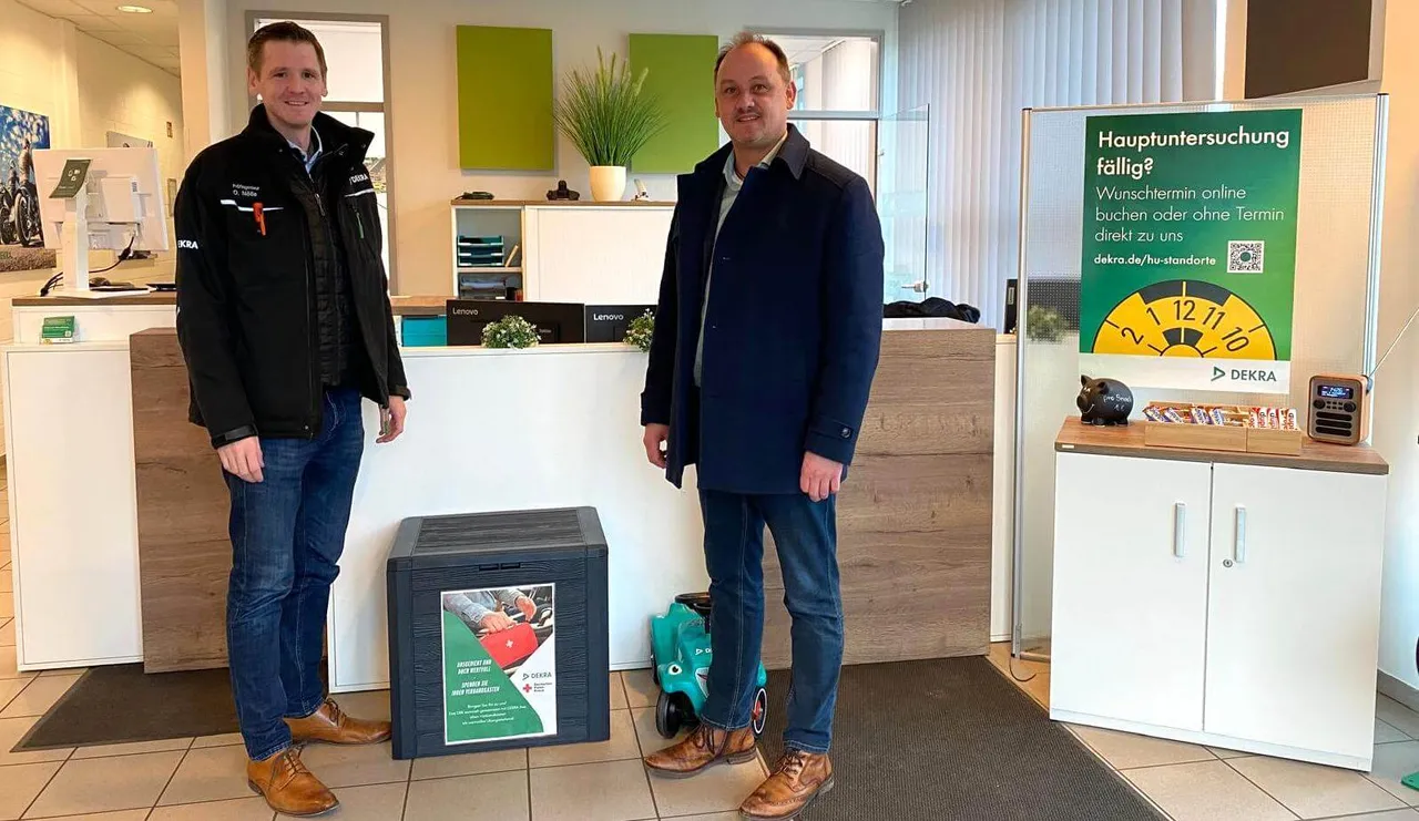 Oliver Nölle und Markus Pflüger stehen neben einer schwarzen Sammelbox für ausgediente Verbandskästen.