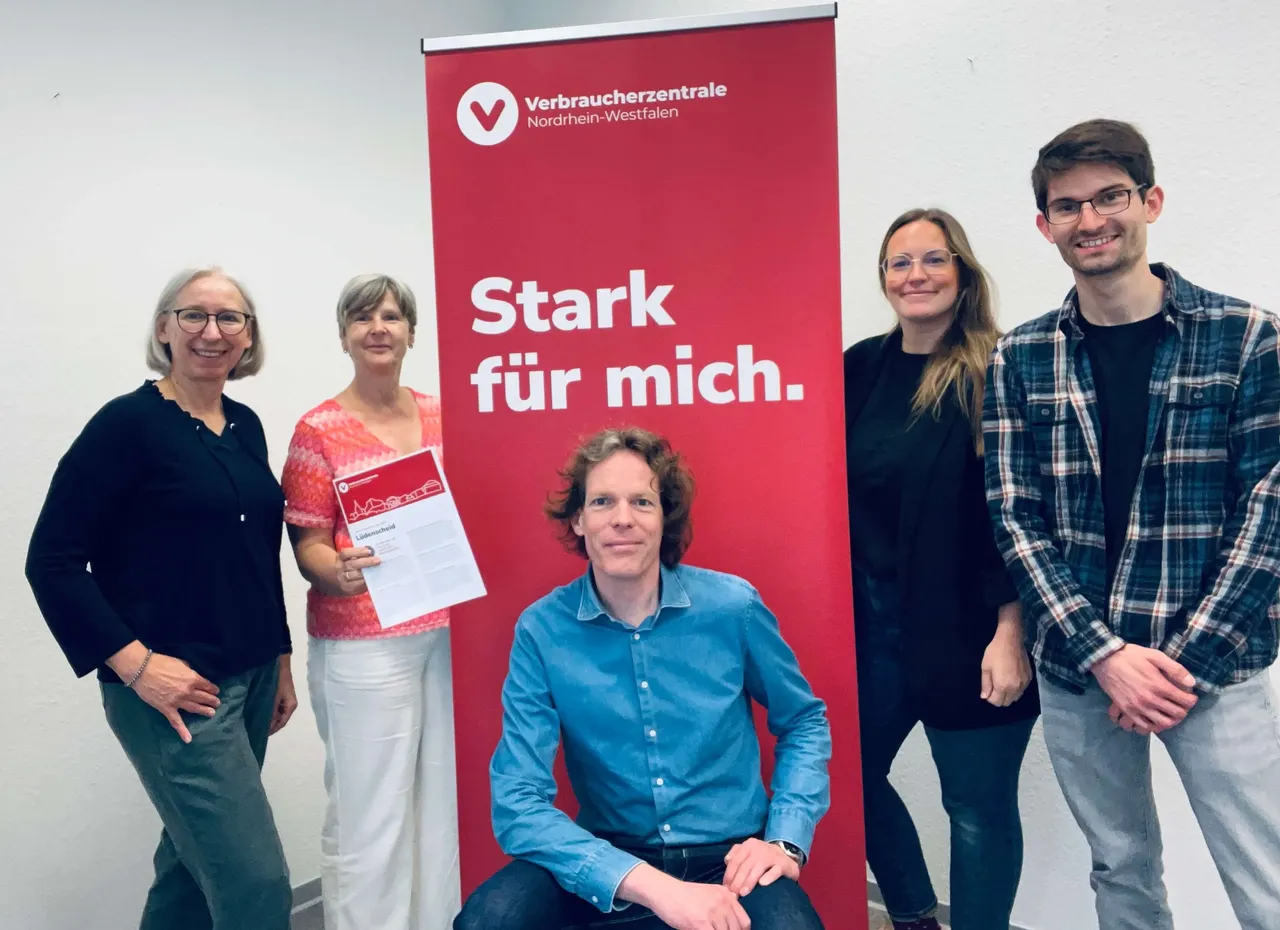 Fünf Mitarbeitende der Verbraucherzentrale Lüdenscheid stehen vor einem Banner mit dem Slogan „Stark für mich.“ und dem Logo der Verbraucherzentrale Nordrhein-Westfalen.