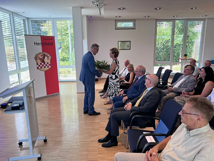 Wolfgang Vöpel erhält bei einer feierlichen Veranstaltung in der Gemeinde Herscheid einen Blumenstrauß von einer Frau.