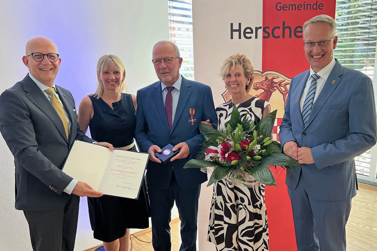 Wolfgang Vöpel steht mit vier Personen bei der Verleihung des Verdienstkreuzes. Er hält eine blaue Schatulle, ein Mann eine Urkunde und eine Frau einen Blumenstrauß.
