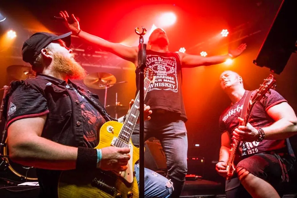 Zwei Musiker auf der Bühne: Links spielt ein Mann mit Bart Gitarre, rechts singt ein Mann mit hoch erhobenen Armen ins Mikrofon.