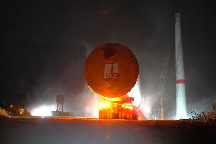 Ein orangefarbenes Turmsegment einer Windkraftanlage wird nachts auf einem Lastwagen transportiert.