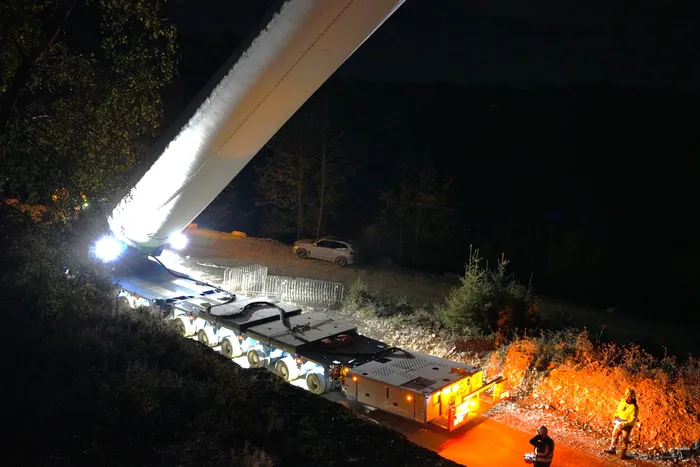 Ein weißer Turmabschnitt einer Windkraftanlage wird nachts auf einem Schwerlasttransporter transportiert.