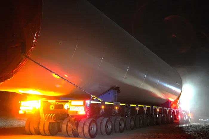 Nachttransport eines großen, grauen Turmsegments für eine Windkraftanlage auf einem mehrachsigen Schwerlasttransporter.