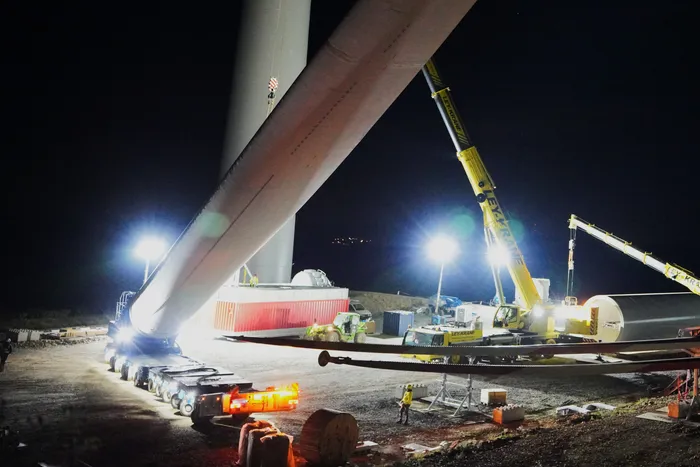 Ein großes Rotorblatt einer Windkraftanlage auf einem mehrachsigen Schwerlasttransporter bei Nacht.