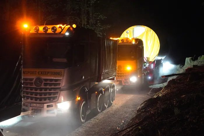 Ein Lastwagen transportiert bei Nacht ein großes, gelbes, kreisförmiges Turmelement für eine Windenergieanlage.