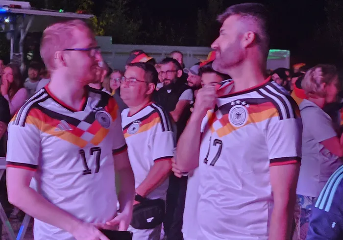 Zwei Männer im deutschen Fußballtrikot mit der Nummer 17 schauen während einer Public-Viewing-Veranstaltung angespannt nach vorn. Im Hintergrund sind weitere Zuschauer zu sehen.