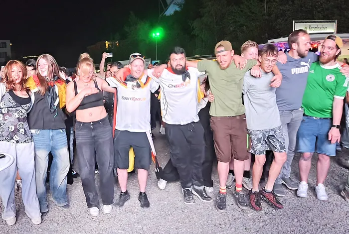 Eine Gruppe von Fans umarmt sich und zeigt ihre Enttäuschung nach einem Fußballspiel. Im Hintergrund ist ein Werbeschild für 