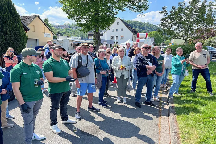 Menschen stehen auf einer Straße und blicken auf ein festlich geschmücktes Gebäude im Hintergrund, während ein Mann mit Handschuhen im Vordergrund steht.