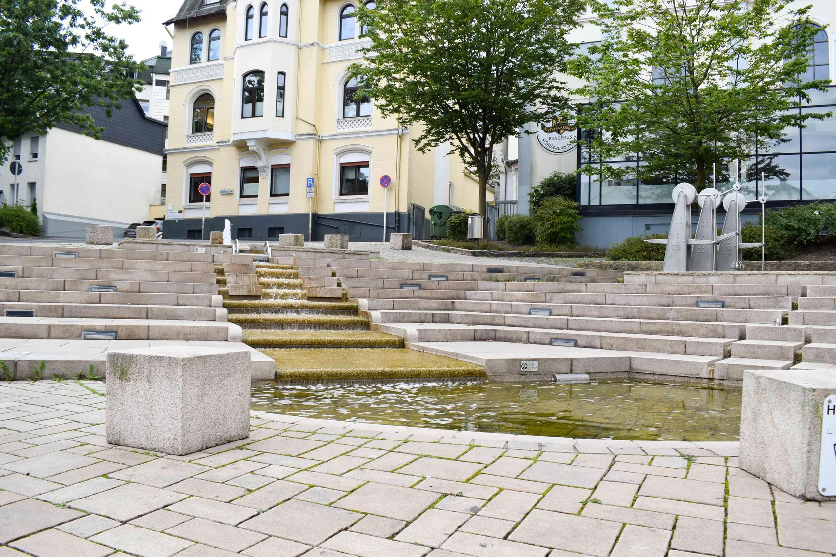 Mehrstufiger Brunnen mit fließendem Wasser im Rosengarten, im Hintergrund ein helles Gebäude mit vielen Fenstern.