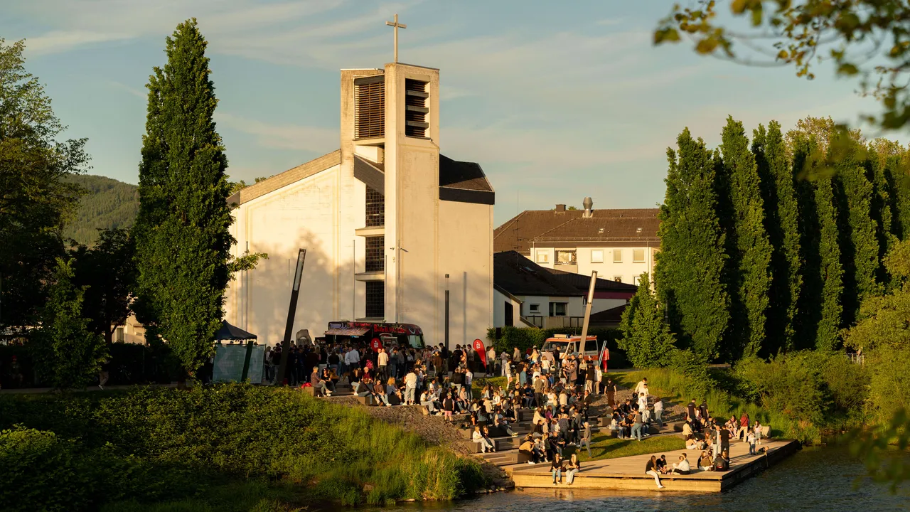 Die KulTour GmbH veranstaltet einen Sommerabend an der Lenne mit Besuchern vor einer modernen Kirche und Foodtrucks.