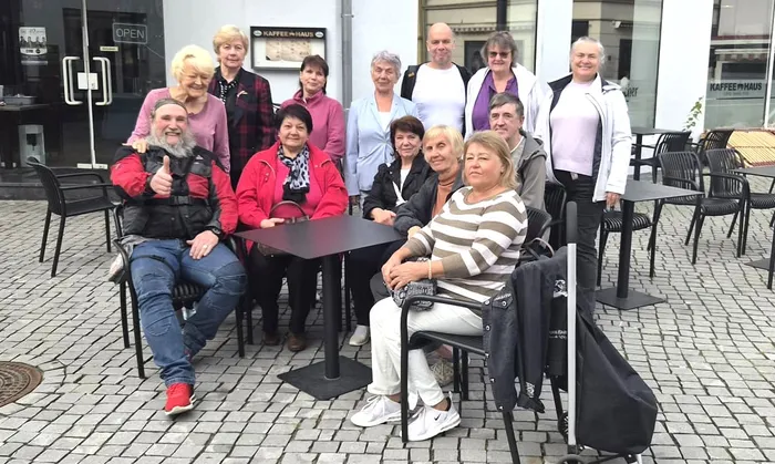 Eine Gruppe von Menschen sitzt und steht gemeinsam an Tischen im Außenbereich eines Cafés.