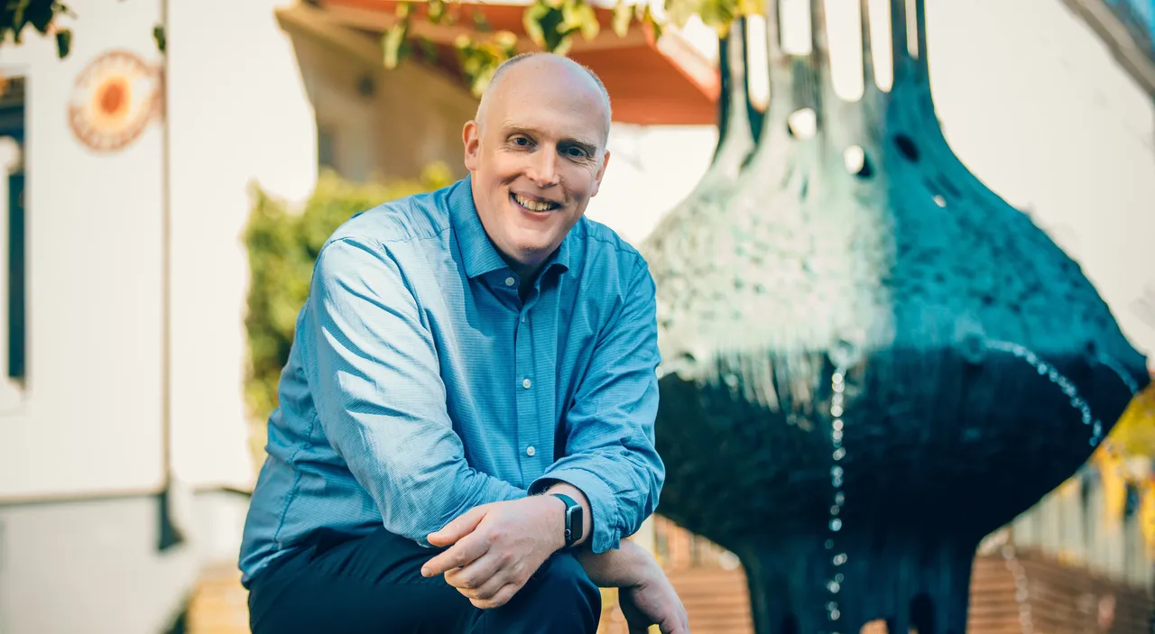 Christoph Weiland, CDU-Vorsitzender, lächelt in die Kamera, neben einer modernen Skulptur mit Wasserfall.