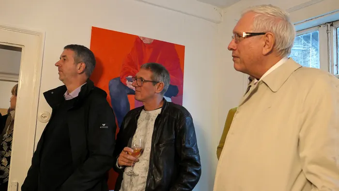 Drei Männer stehen bei der Vernissage der Ausstellung „Zeitmangelwesen“ vor einem großformatigen roten Gemälde.