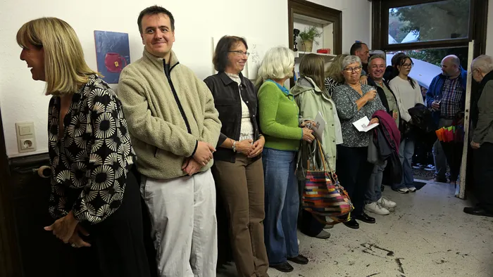 Eine Gruppe von Gästen steht bei der Vernissage der Ausstellung „Zeitmangelwesen“ in einem hellen Raum.
