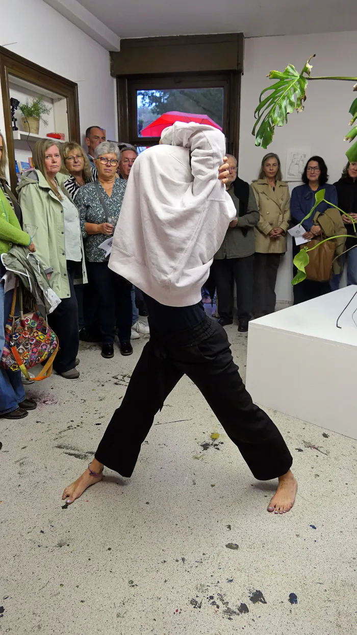 Eine Person in weißem Hoodie und schwarzer Hose vollführt eine Performance vor einer Gruppe von Gästen in einem Ausstellungsraum.