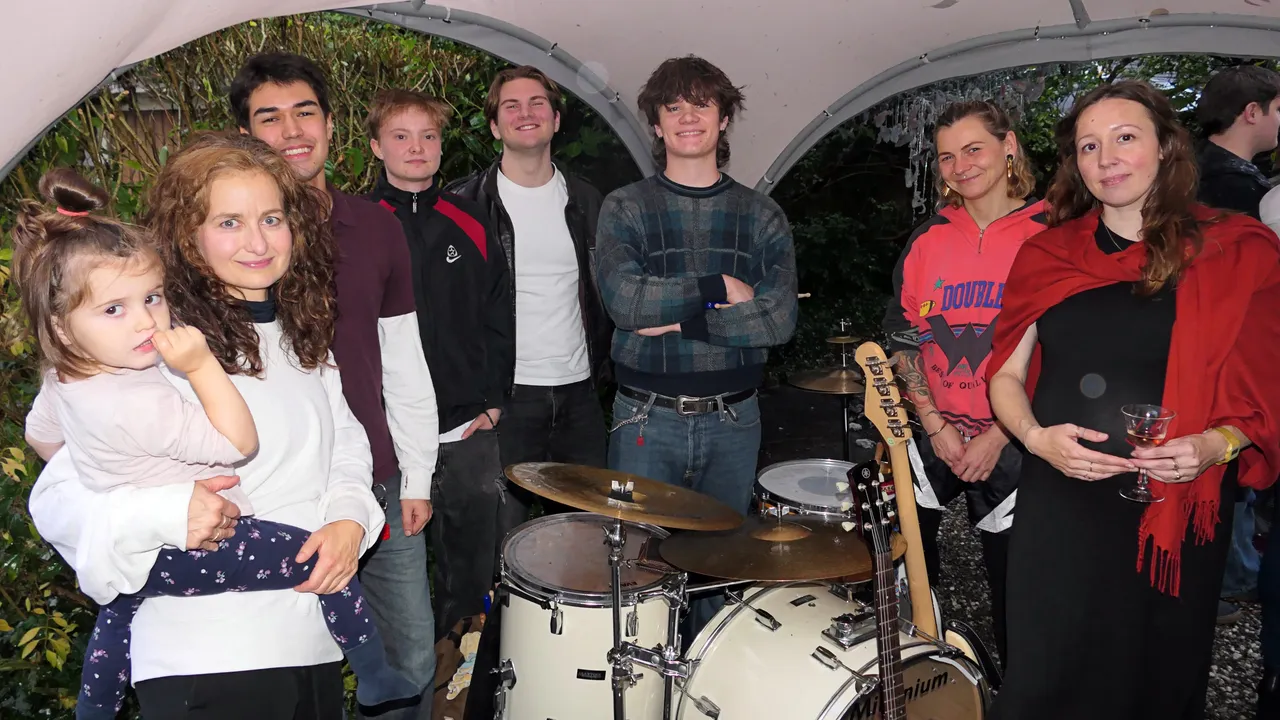 Eine Gruppe von Menschen steht bei der Vernissage der Ausstellung „Zeitmangelwesen“ neben einem Schlagzeug und einer Gitarre.