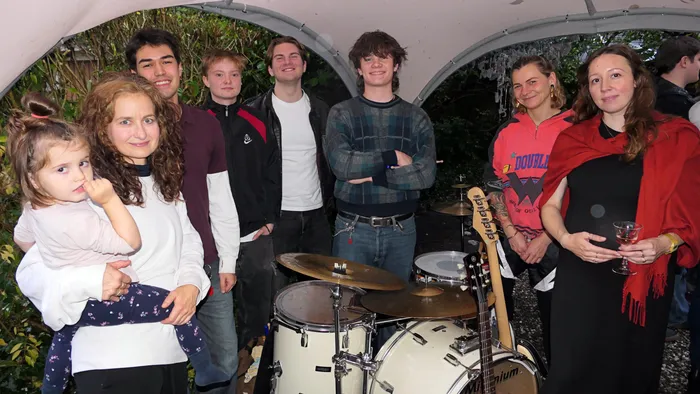 Eine Gruppe von Menschen steht bei der Vernissage der Ausstellung „Zeitmangelwesen“ neben einem Schlagzeug und einer Gitarre.
