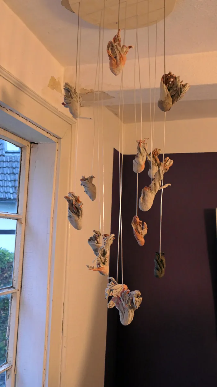 Eine Installation mit organisch geformten, hellen Objekten, die an dünnen Fäden von einer runden Deckenhalterung herabhängen.