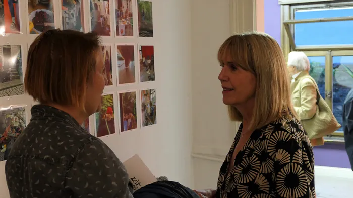Anja Herzog und Helena Zubler im Gespräch vor einer Wand mit ausgestellten Fotografien bei ihrer Ausstellung „Zeitmangelwesen“.