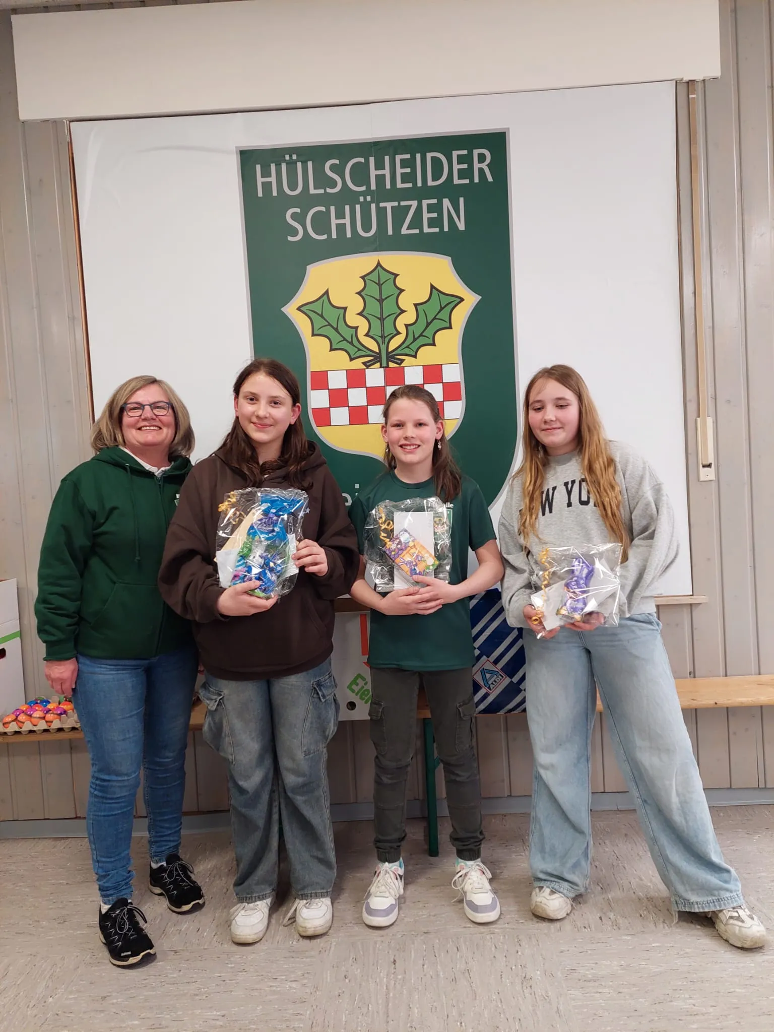 Vier Personen stehen vor einer Wand mit dem Schriftzug „Hülscheider Schützen“. Von links: Konny Krause, Mia Kückelhaus, Isabelle Walkhoff und Anna Thieltges halten jeweils eine mit Süßigkeiten gefüllte Tüte.