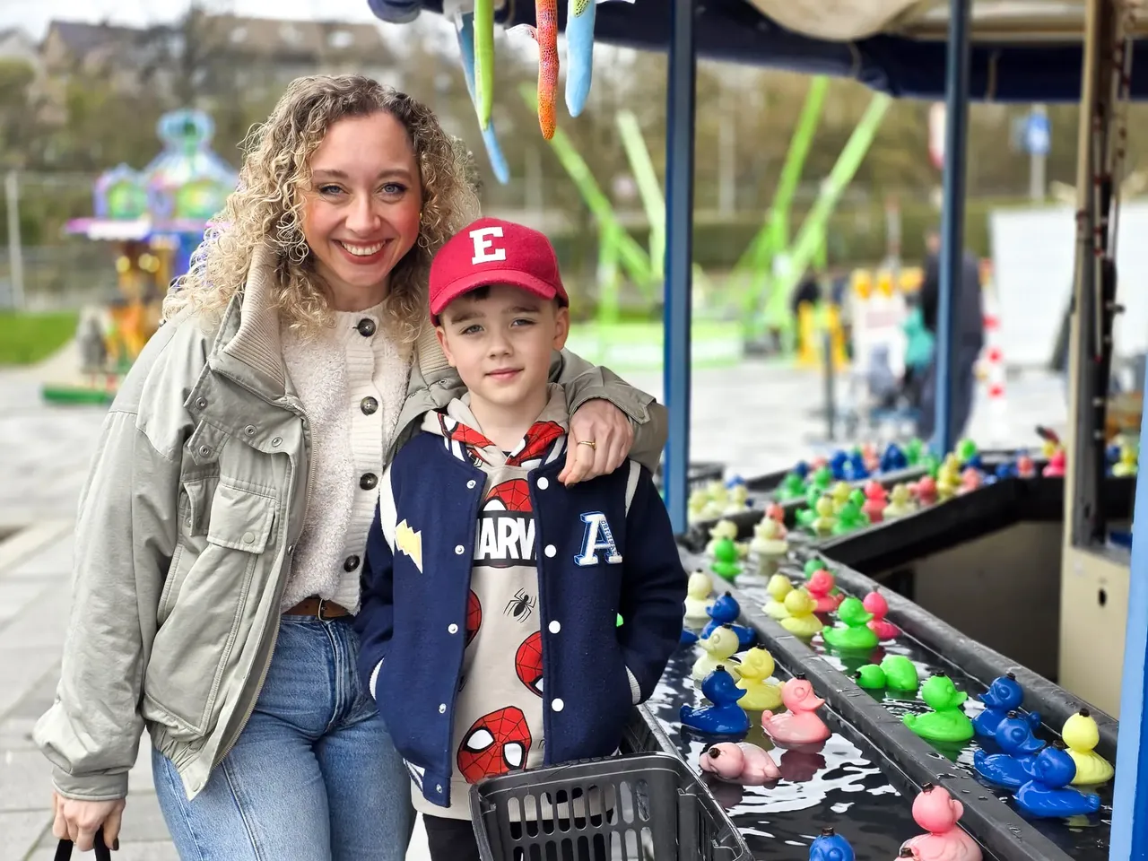 Eine Frau mit lockigem Haar und ein kleiner Junge mit roter Kappe stehen vor einem Entenfangbecken auf der Osterkirmes in Meinerzhagen.