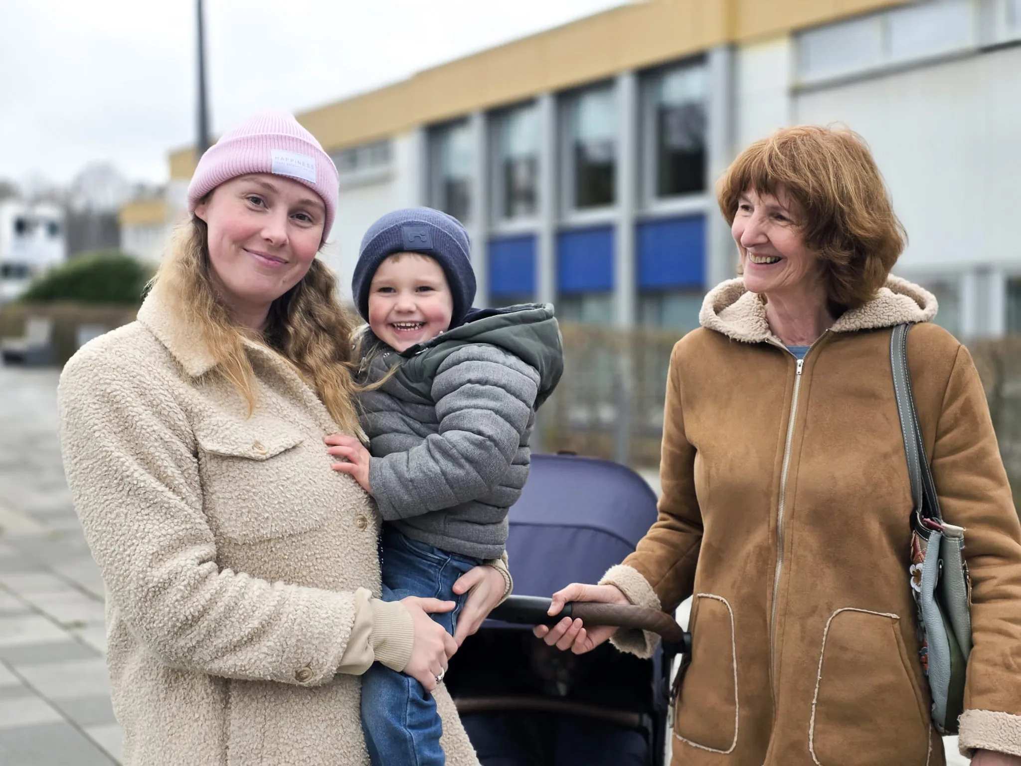 Drei Generationen – eine junge Frau, ein Kleinkind und eine ältere Frau – stehen lächelnd vor einem hellen Gebäude, vermutlich auf der Osterkirmes in Meinerzhagen.