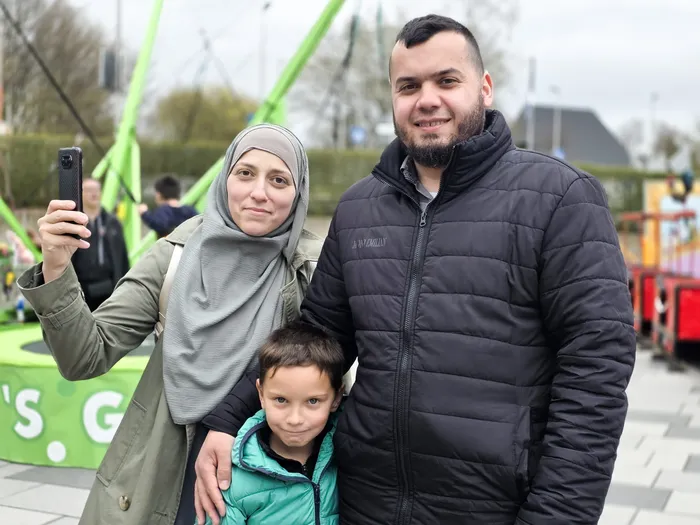 Familie mit Kind macht ein Selfie vor dem Hintergrund einer Kirmesattraktion.