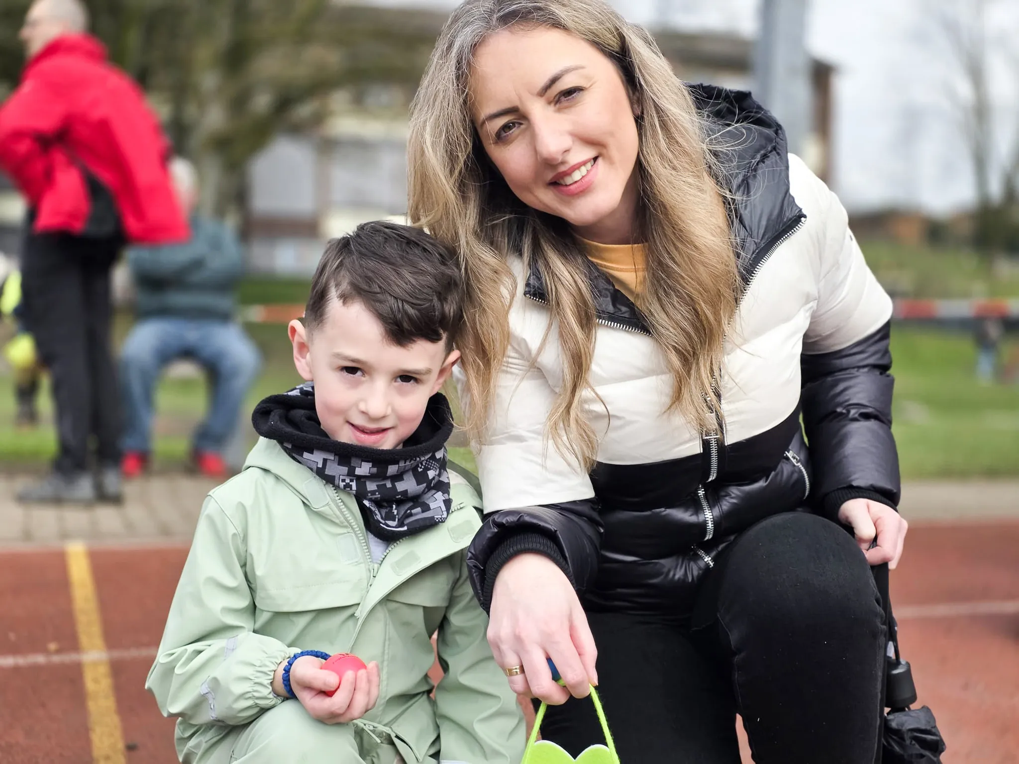 Eine Frau und ein Junge sitzen nebeneinander und lächeln in die Kamera. Sie halten Ostereier in den Händen.