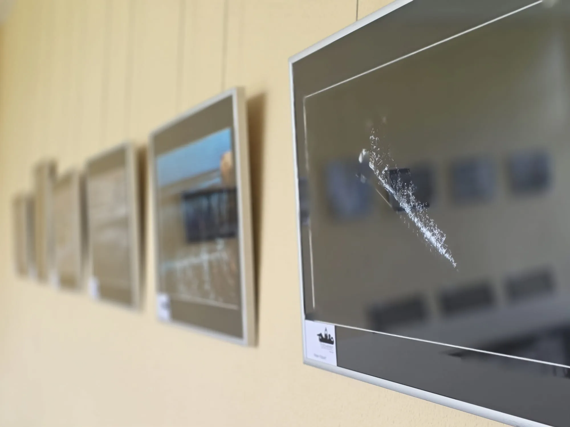 Mehrere gerahmte Fotografien mit Wasser als Thema hängen an einer hellen Wand.