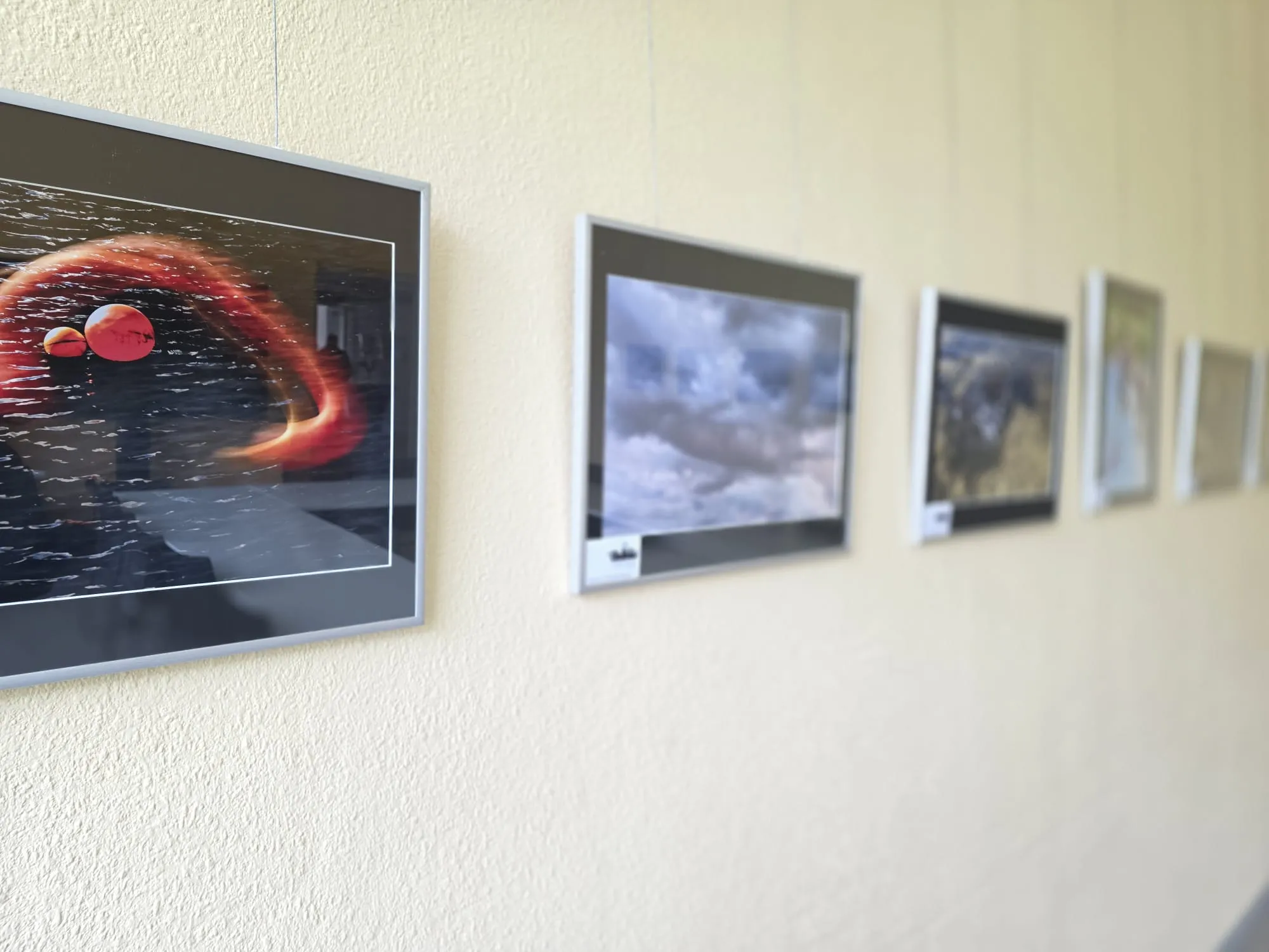 Mehrere gerahmte Fotografien mit Wasser-Motiven hängen an einer hellen Wand in einer Reihe.