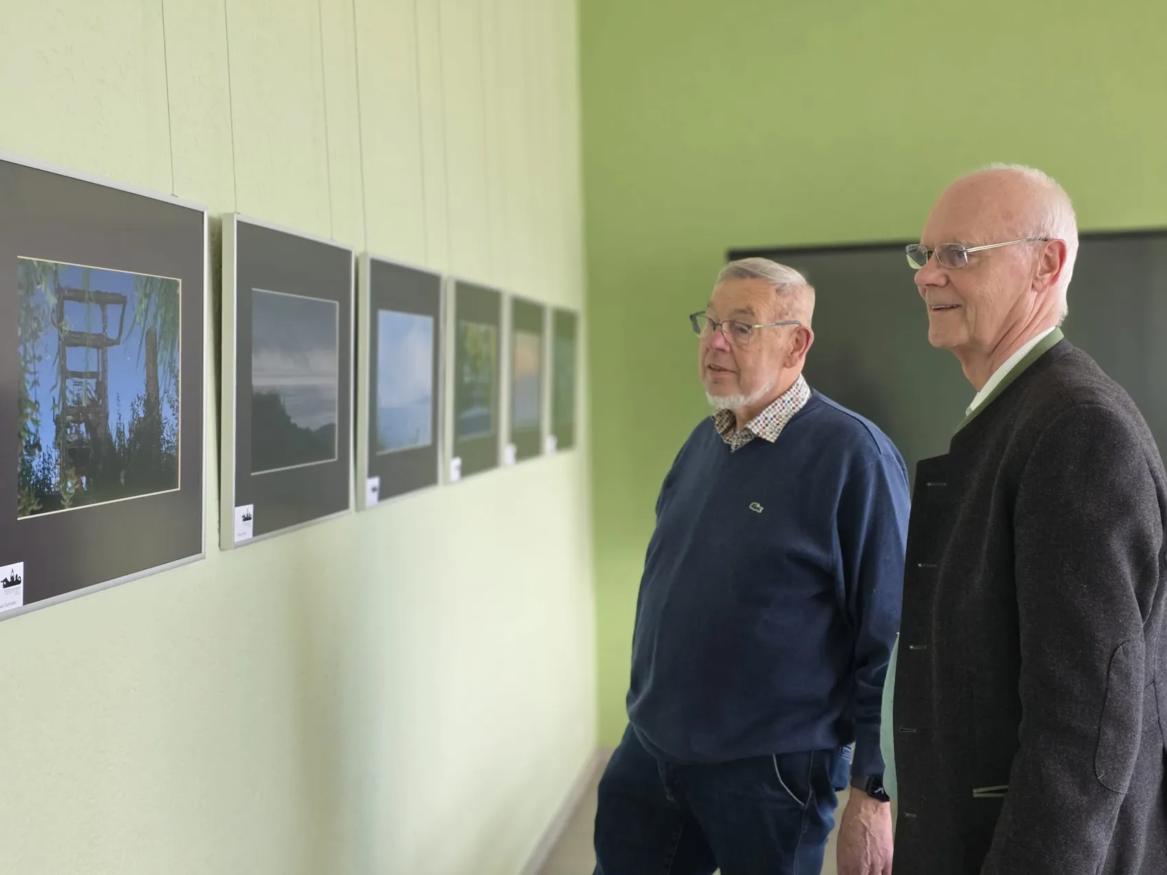 Zwei ältere Männer betrachten Fotos an einer Wand, die das Thema Wasser zeigen.