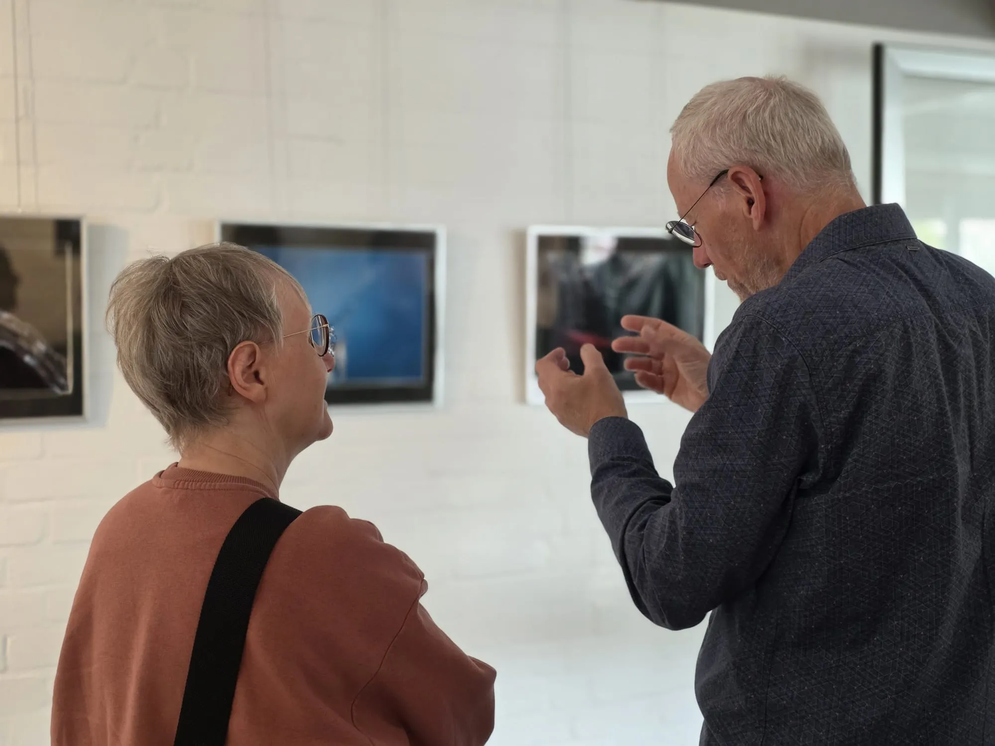 Zwei ältere Menschen betrachten Fotografien mit Wasser-Motiven in einer Galerie.