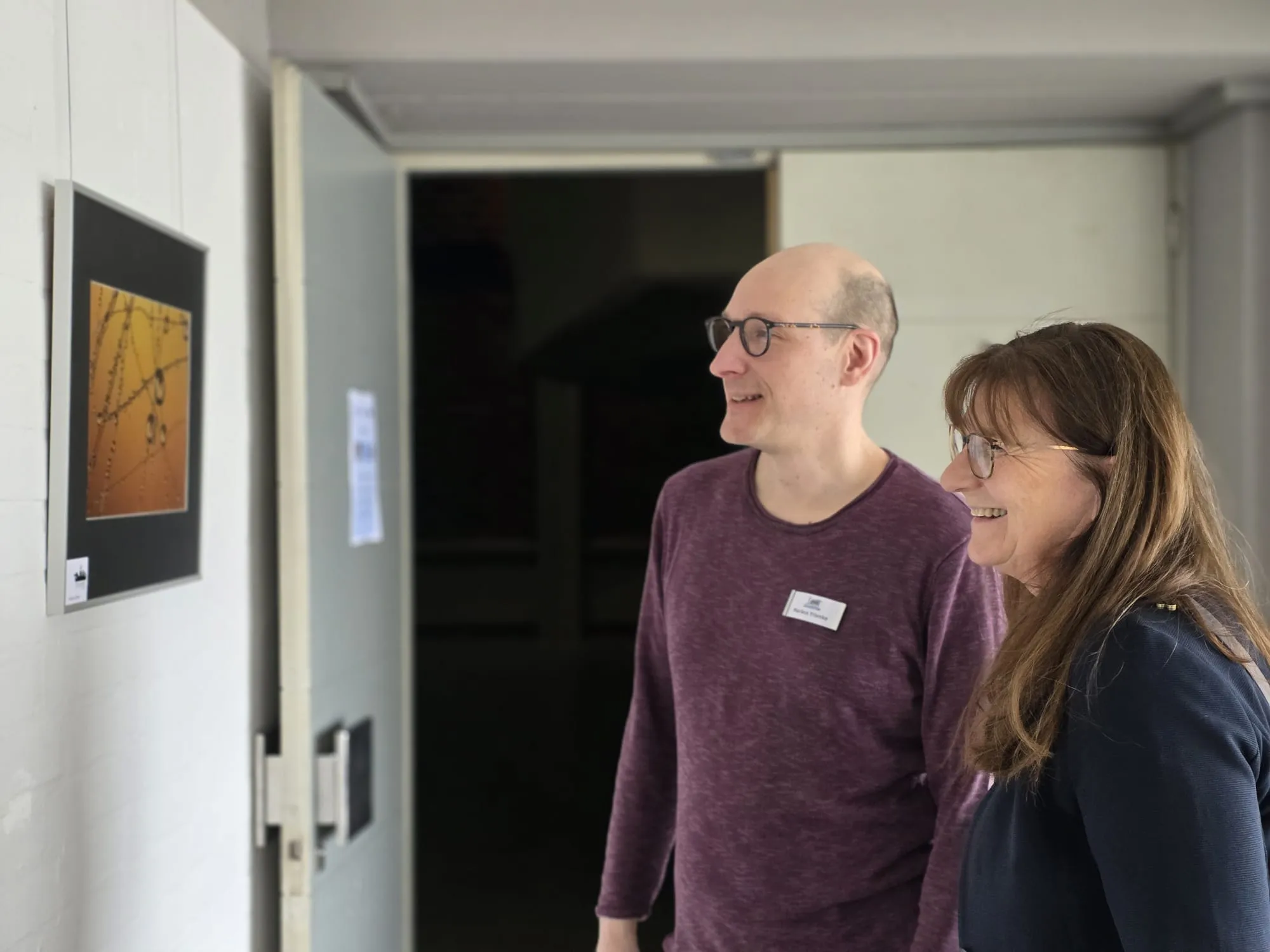 Zwei Personen betrachten ein abstraktes Foto von Wasser an einer Wand in einer Ausstellung.