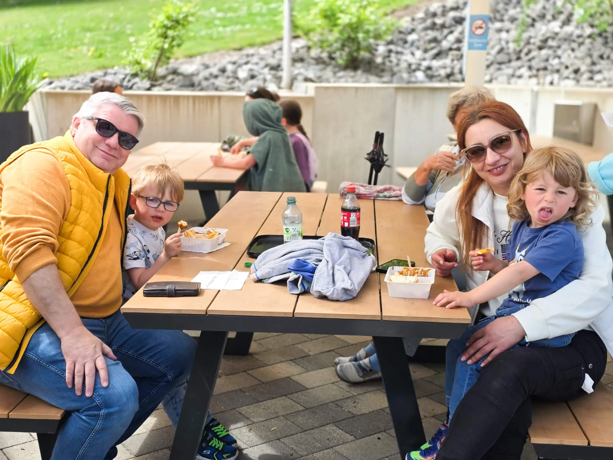 Familie sitzt an einem Picknicktisch und isst Pommes, im Hintergrund weitere Besucher der Saisoneröffnung der Herpine in Halver.