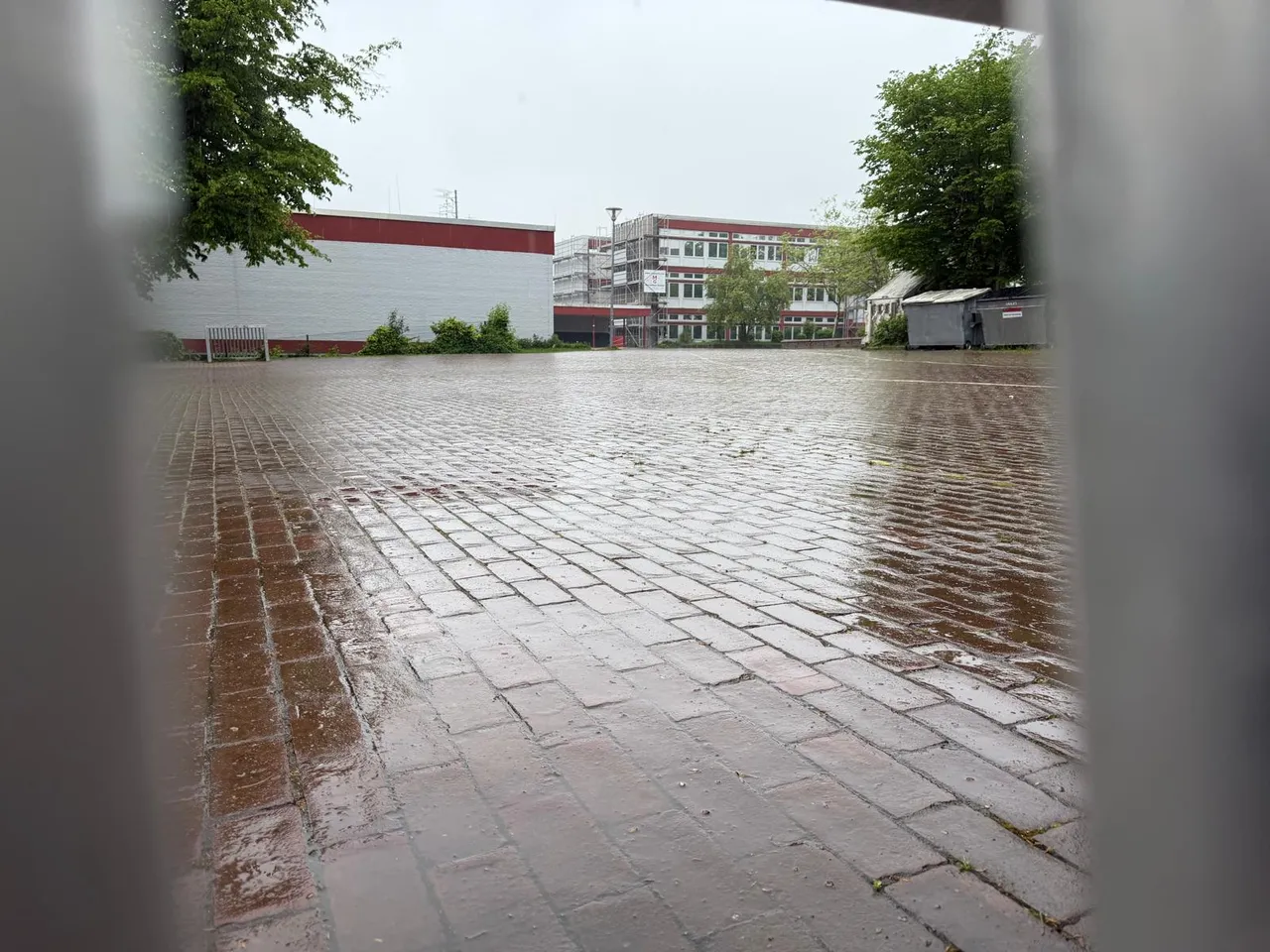 Überschwemmter Schulhof der Gesamtschule Kierspe nach starkem Regen, Gebäude im Hintergrund.