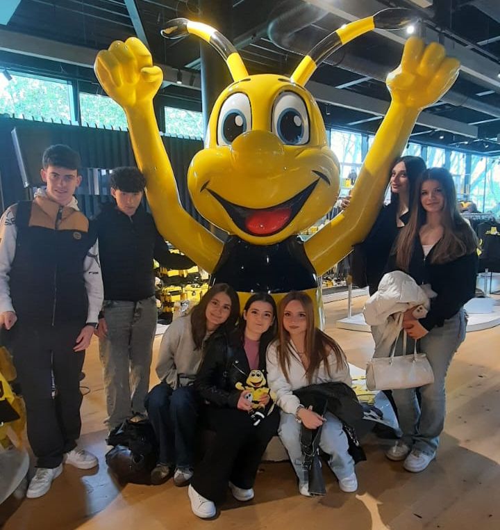 Eine Gruppe Jugendlicher posiert mit dem BVB-Maskottchen Emma, einer großen gelben Biene mit schwarzen Streifen, im Signal Iduna Park. Im Hintergrund sind weitere Personen und die Stadionarchitektur zu sehen.