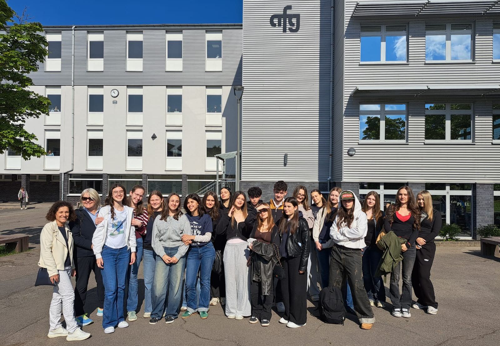 Eine Gruppe von Schülerinnen und Schülern steht vor einem mehrstöckigen Gebäude mit dem Logo „AFG“ auf dem Dach. Sie nehmen an einem Schüleraustausch mit dem Instituto Soleri Bertoni aus Italien teil.