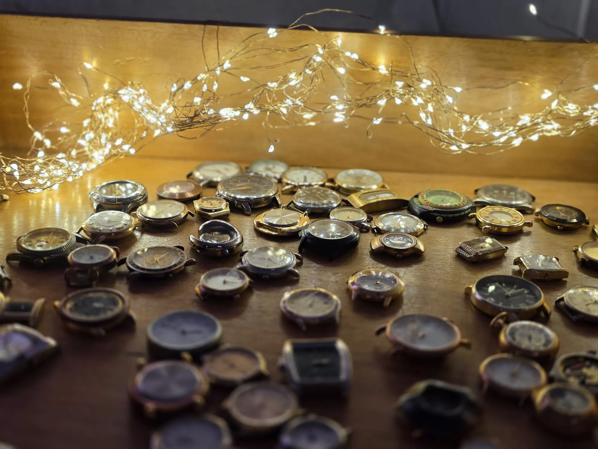Eine Sammlung alter Armbanduhren liegt auf einer Holzoberfläche, beleuchtet von einer Lichterkette. Das Bild steht im Zusammenhang mit dem 50-jährigen Jubiläum der Schule an der Höh.