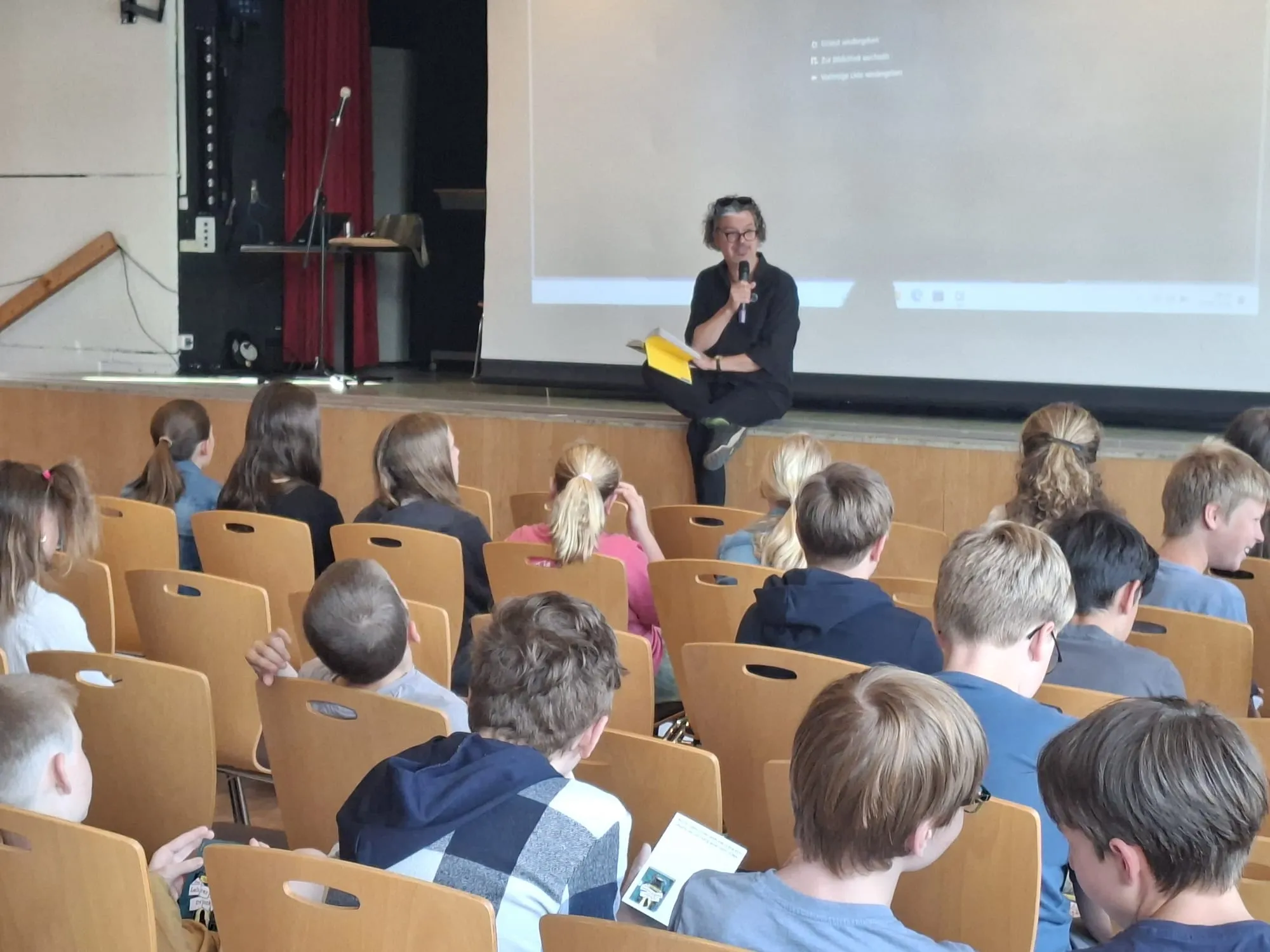 Christian Seltmann liest aus seinem Buch vor einer Gruppe Schüler in einem Auditorium.