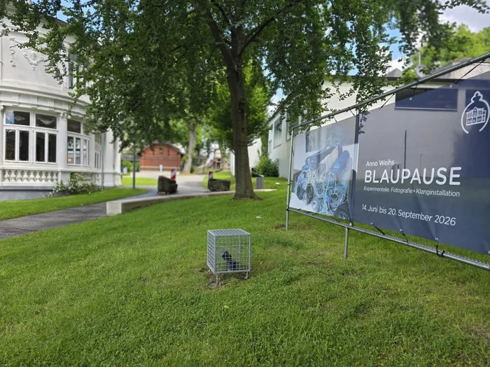 Anno Weihs’ Ausstellung „BLAUPARUSE“ wird in einem Banner vor der Villa Wippermann beworben, das experimentelle Fotografie und Klanginstallationen zeigt. Die Ausstellung läuft vom 14. Juni bis zum 20. September 2026.