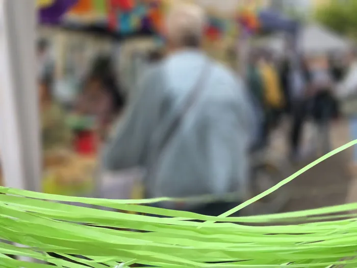 Menschen stehen unscharf im Hintergrund eines Sommerfestes, im Vordergrund grüne Papierstreifen.